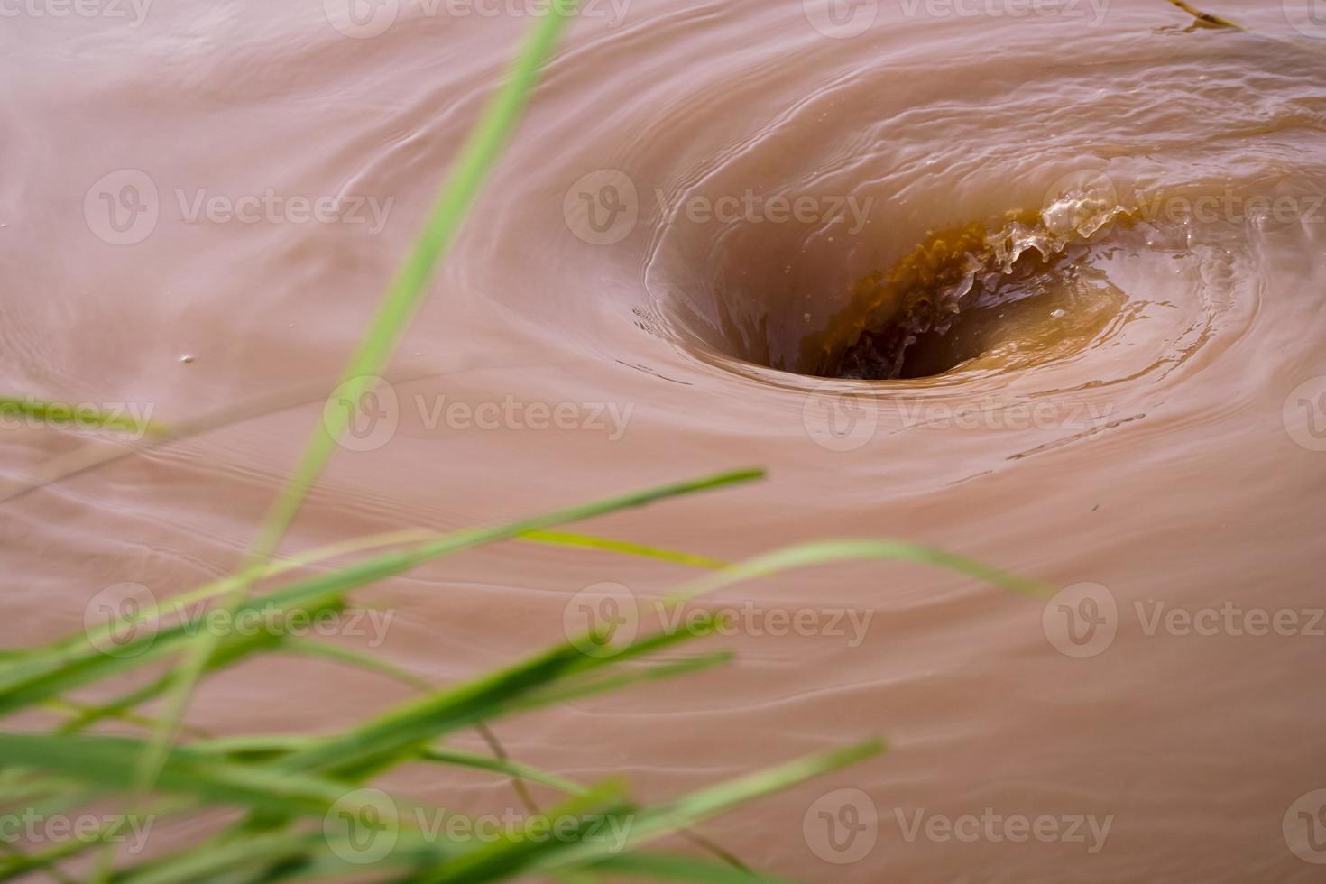 se crea un poderoso vórtice en la superficie verde del río que fluye vigorosamente por las lluvias torrenciales y las inundaciones. foto