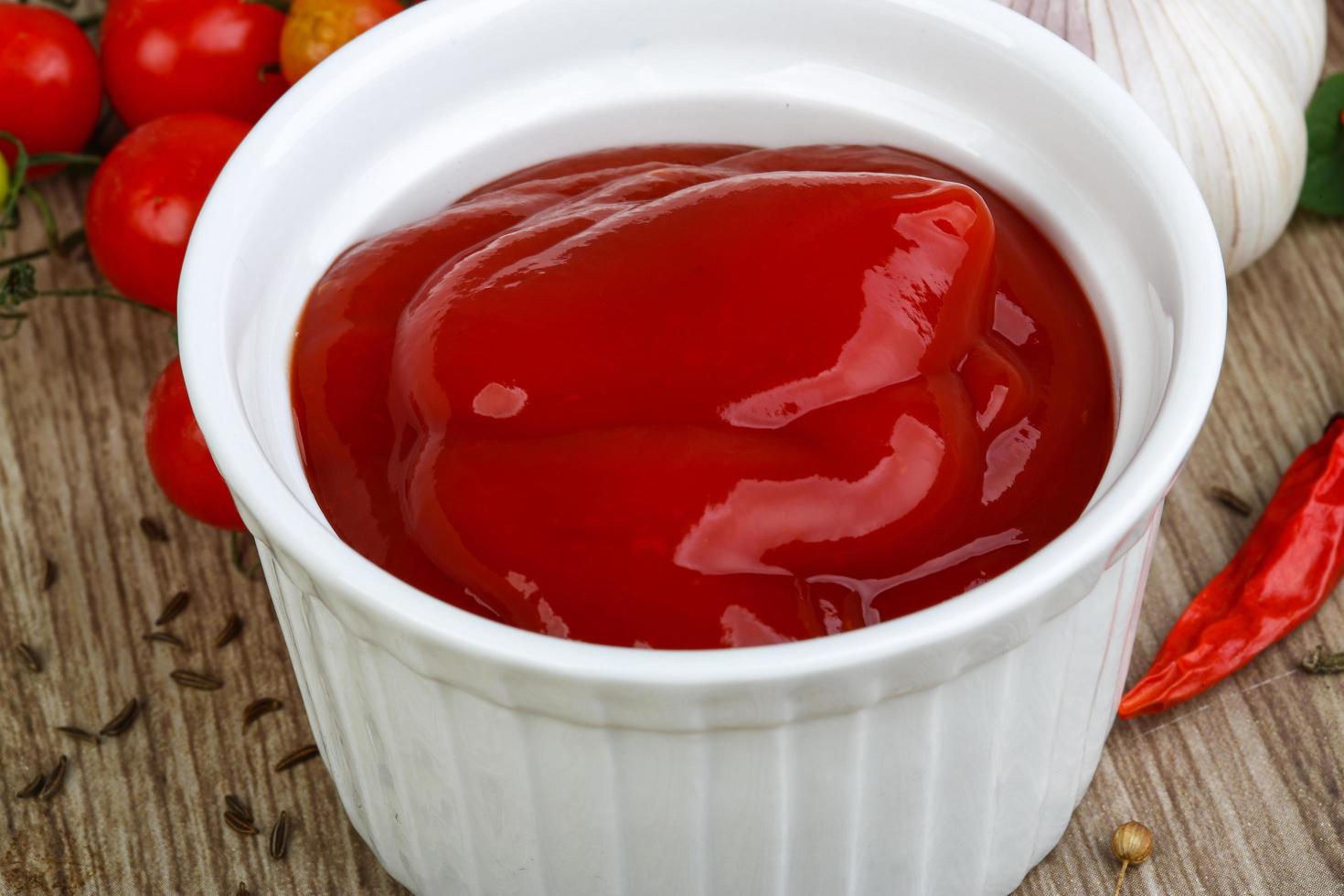 ketchup de tomate en un recipiente sobre fondo de madera foto