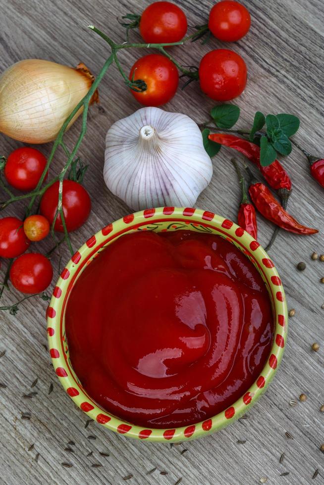 ketchup de tomate en un recipiente sobre fondo de madera foto