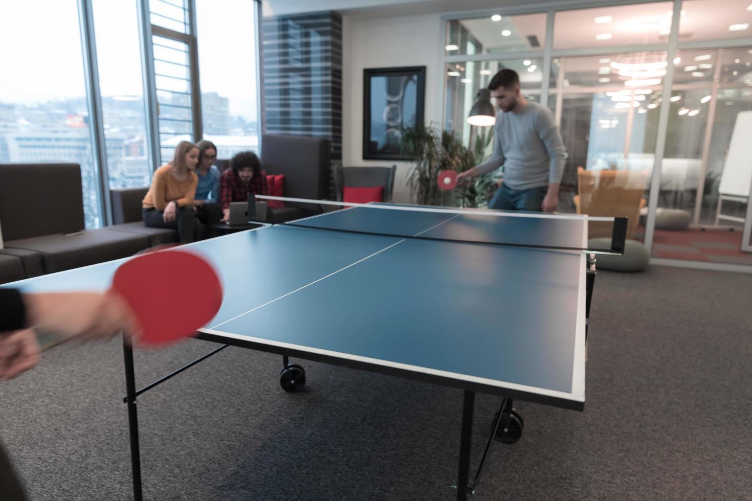 Two young start up business man playing table tennis at modern creative office space people group have meeting and brainstorming in background photo