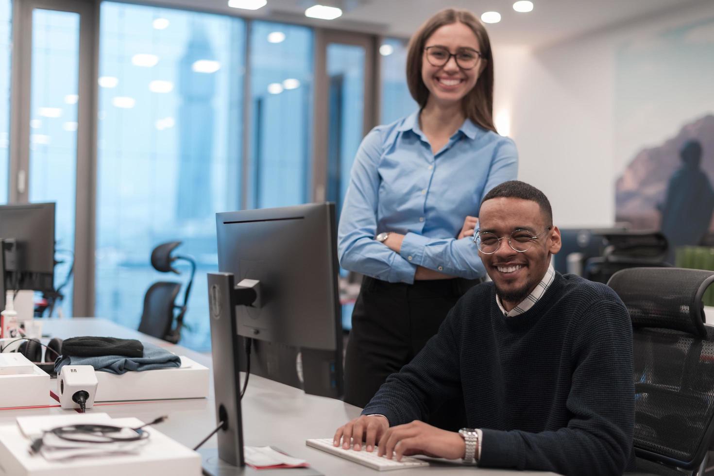 Young smiling woman explaining to serious African American coworker project strategy. Diverse startup coworkers students woman and man talking discussing working in modern office using computer. photo
