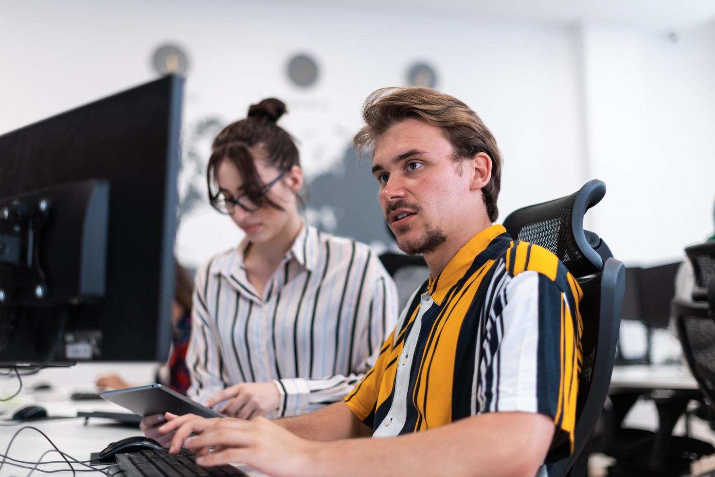 Business couple working together on project using tablet and desktop computer at modern open plan startup office. Selective focus photo