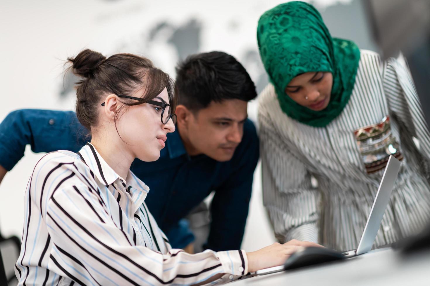 Multiethnic startup business team Arabian woman wearing a hijab on meeting in modern open plan office interior brainstorming, working on laptop and desktop computer. Selective focus photo