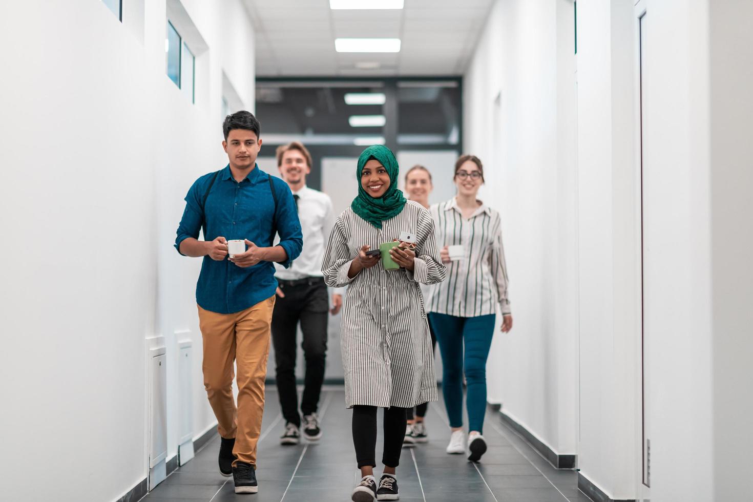 equipo empresarial multiétnico caminando por el pasillo del edificio mientras regresa de un descanso para tomar café foto