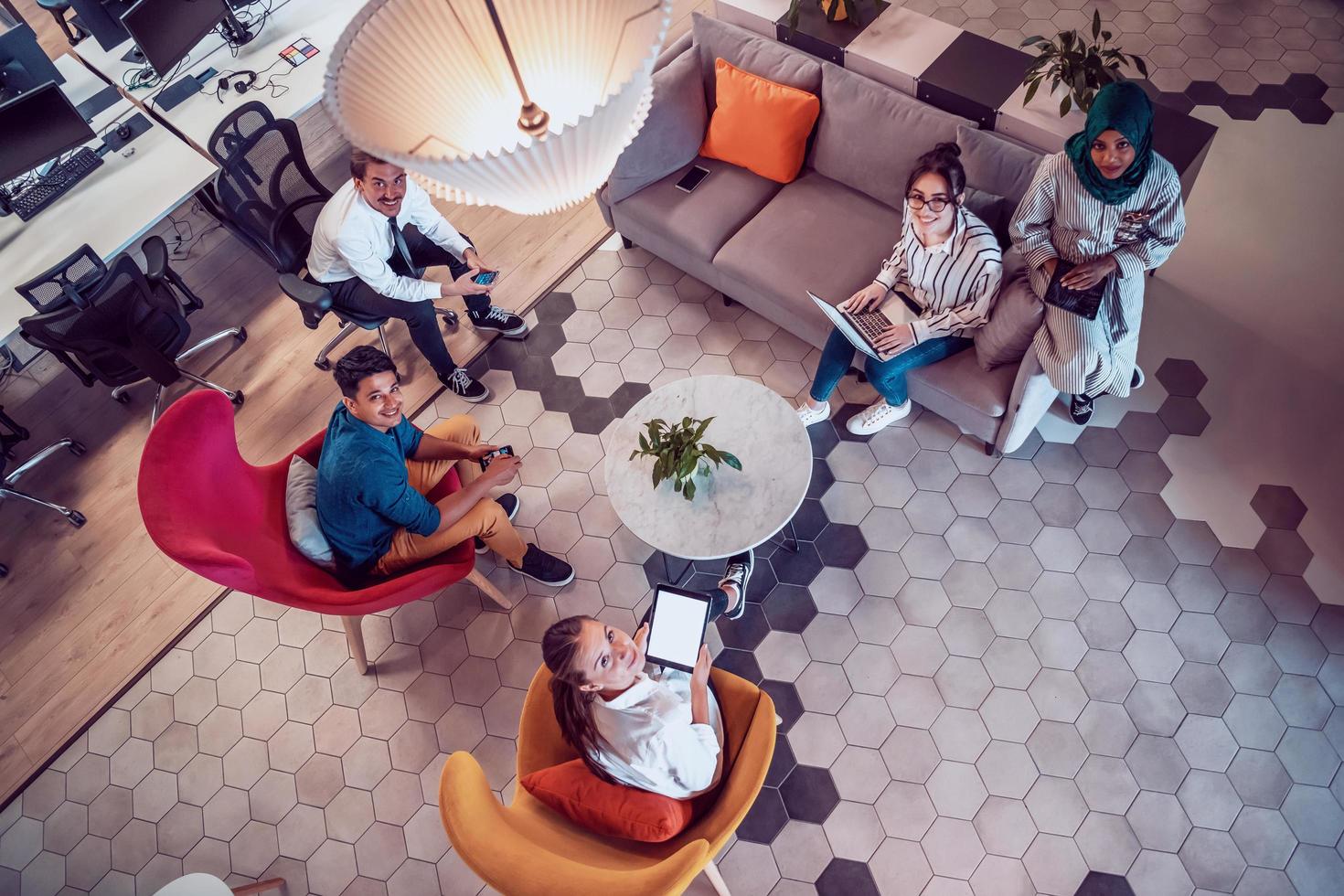 Top view photo of Multiethnic startup business team having brainstorming in relaxation area of modern office interior working on laptop and tablet computer