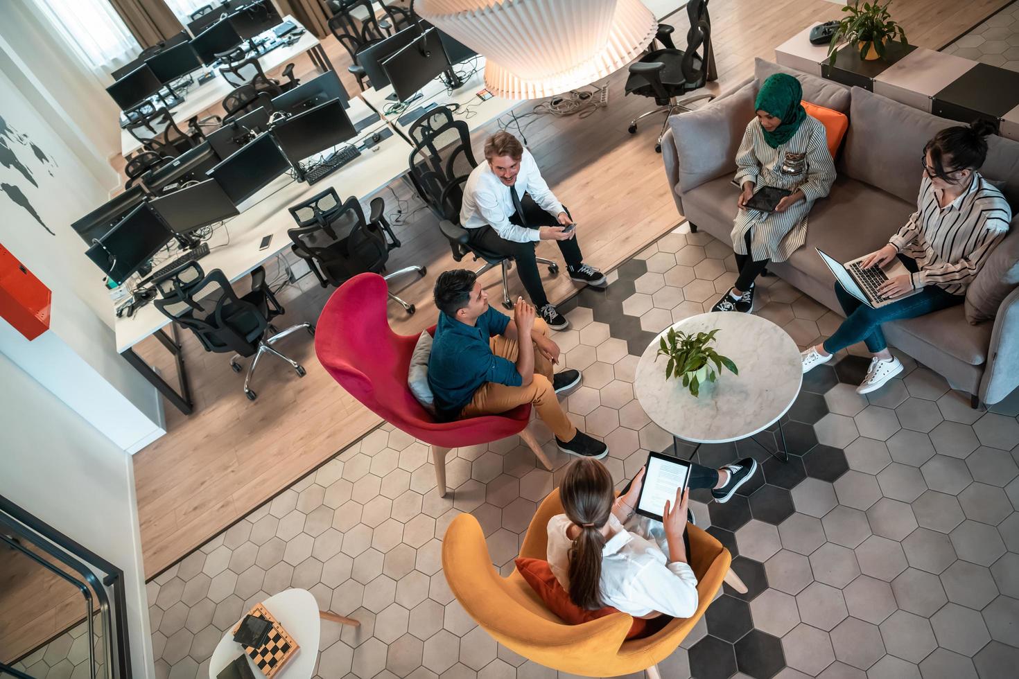Top view photo of Multiethnic startup business team having brainstorming in relaxation area of modern office interior working on laptop and tablet computer