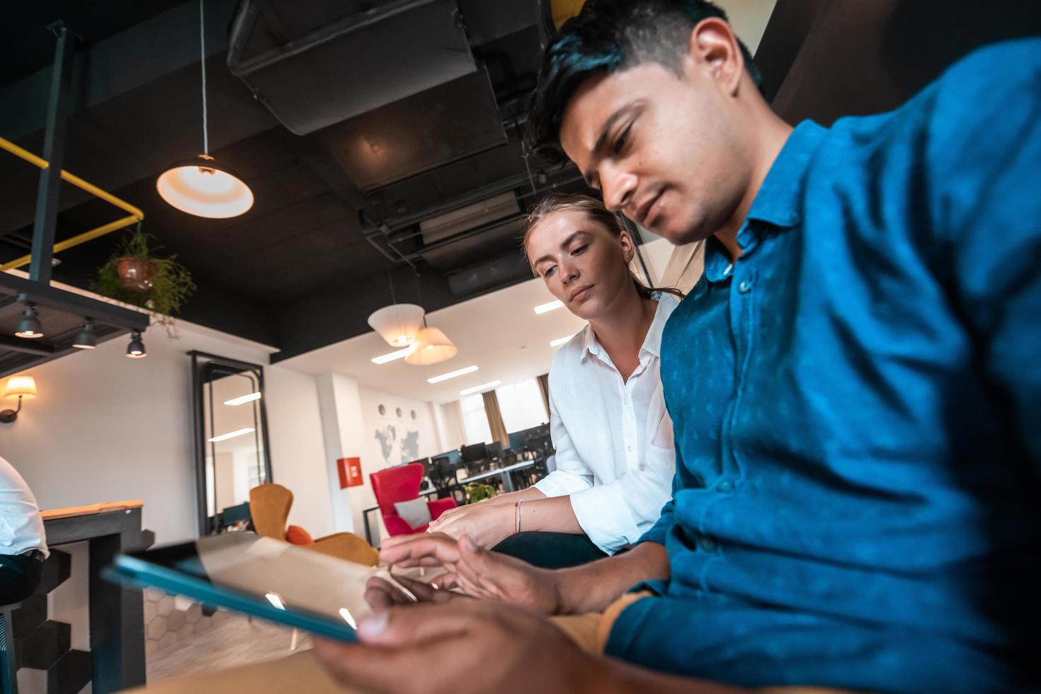 Multiethnic business people man with a female colleague working together on tablet computer in relaxation area of modern startup office photo