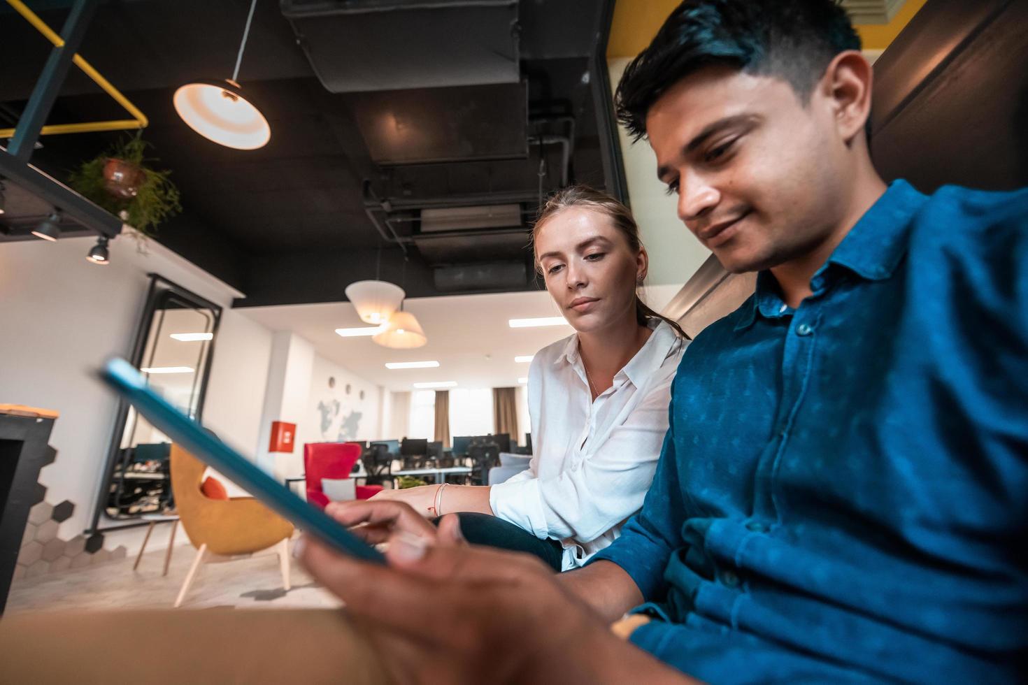 Multiethnic business people man with a female colleague working together on tablet computer in relaxation area of modern startup office photo