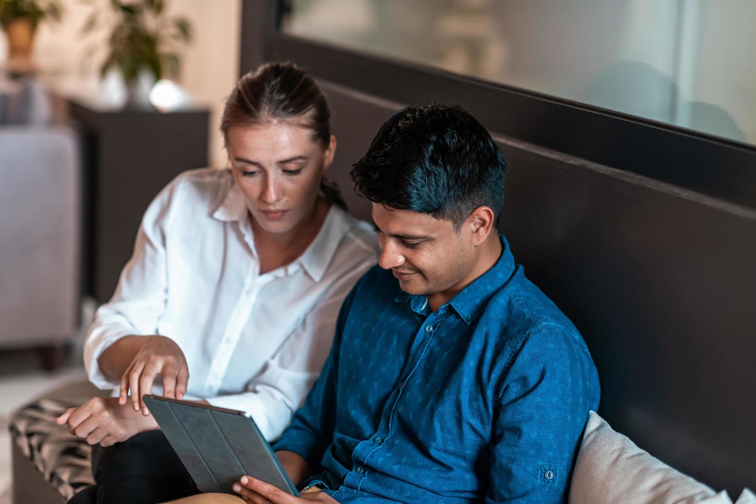 Multiethnic business people man with a female colleague working together on tablet computer in relaxation area of modern startup office photo