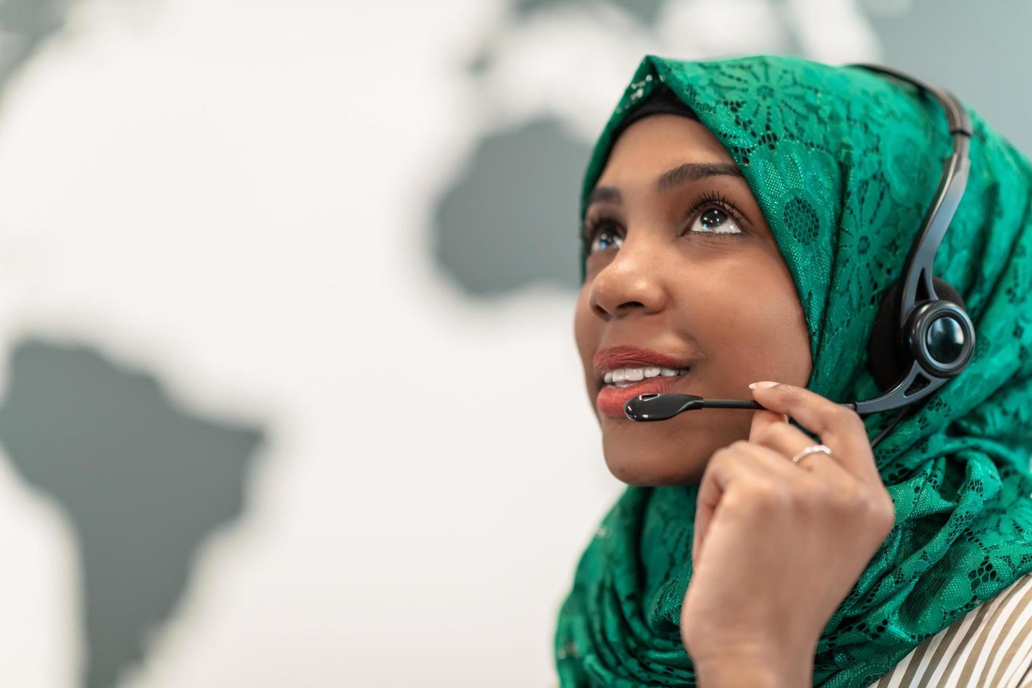 Afro Muslim female with green hijab scarf customer representative business woman with phone headset helping and supporting online with customer in modern call centre photo