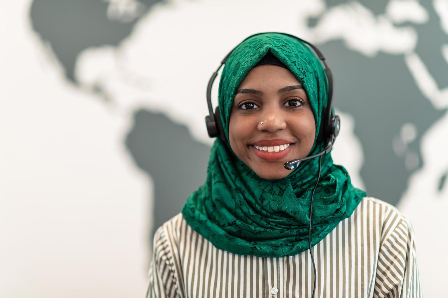 Afro Muslim female with green hijab scarf customer representative business woman with phone headset helping and supporting online with customer in modern call centre photo