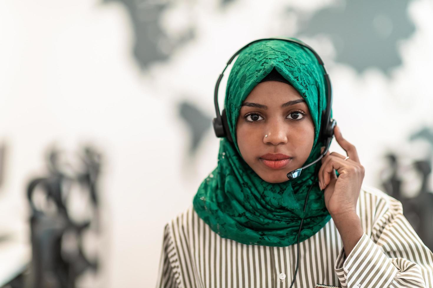 Afro Muslim female with green hijab scarf customer representative business woman with phone headset helping and supporting online with customer in modern call centre photo