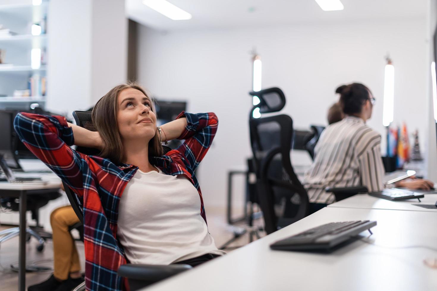 Casual business woman taking a break while working on desktop computer in modern open plan startup office interior. Selective focus photo