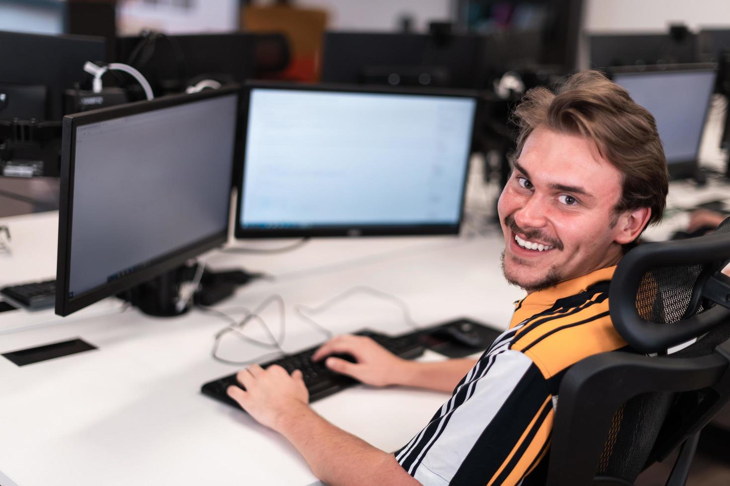 Casual man working on desktop computer in modern open plan startup office interior. Selective focus photo