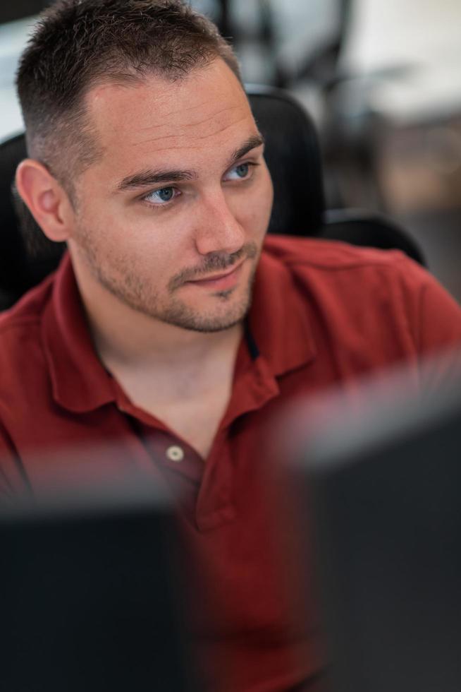 Casual business man working on desktop computer in modern open plan startup office interior. Selective focus photo