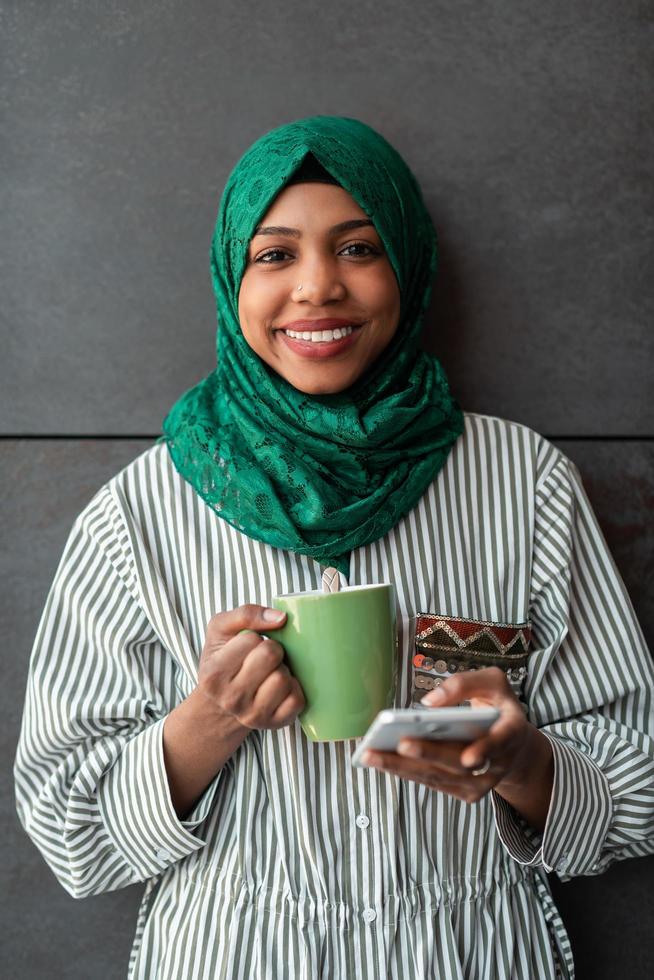 African Muslim businesswoman with green hijab using mobile phone during coffee break from work outside photo