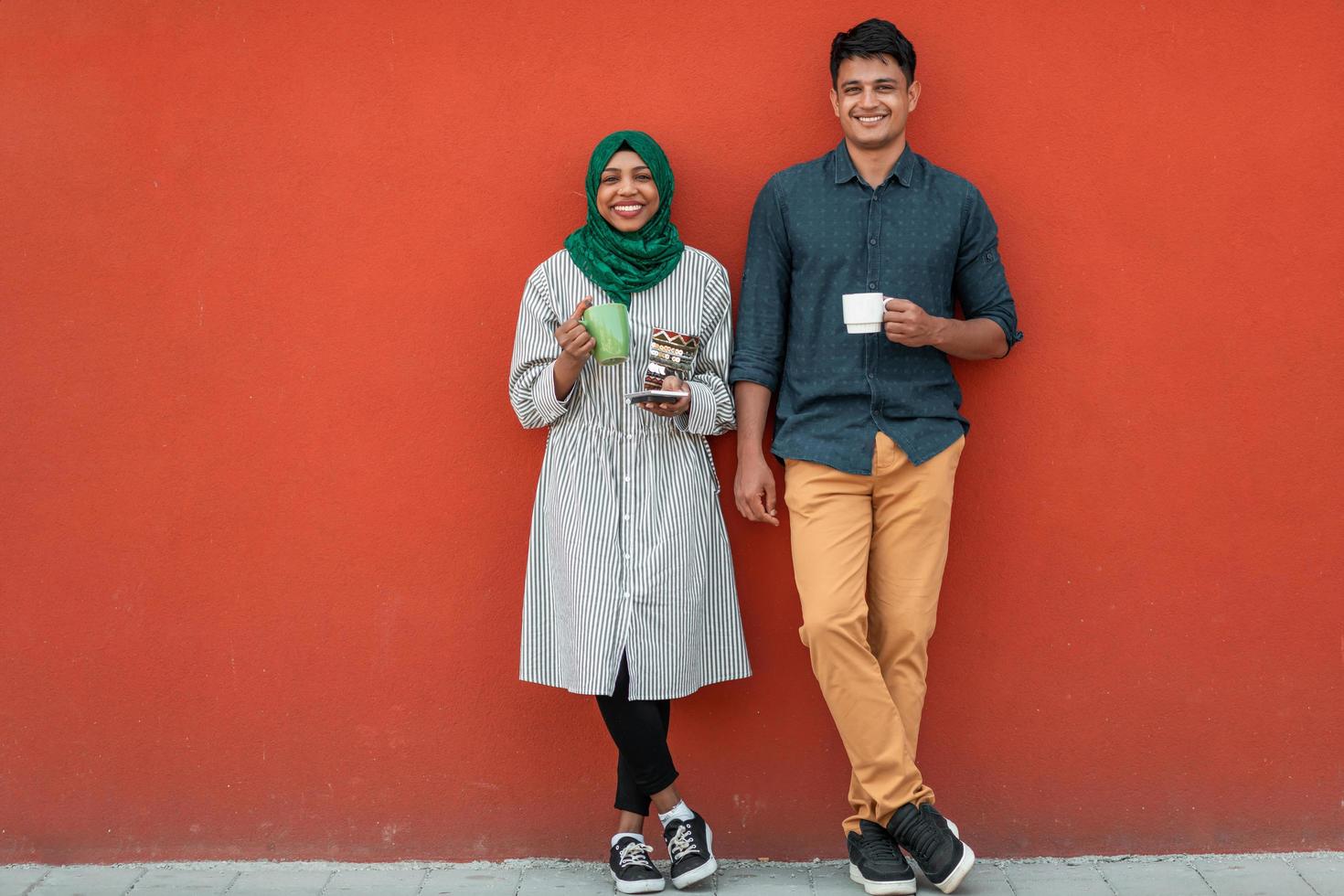 Multiethnic group of casual business people using smartphone during coffee break from work in front of red wall outside photo