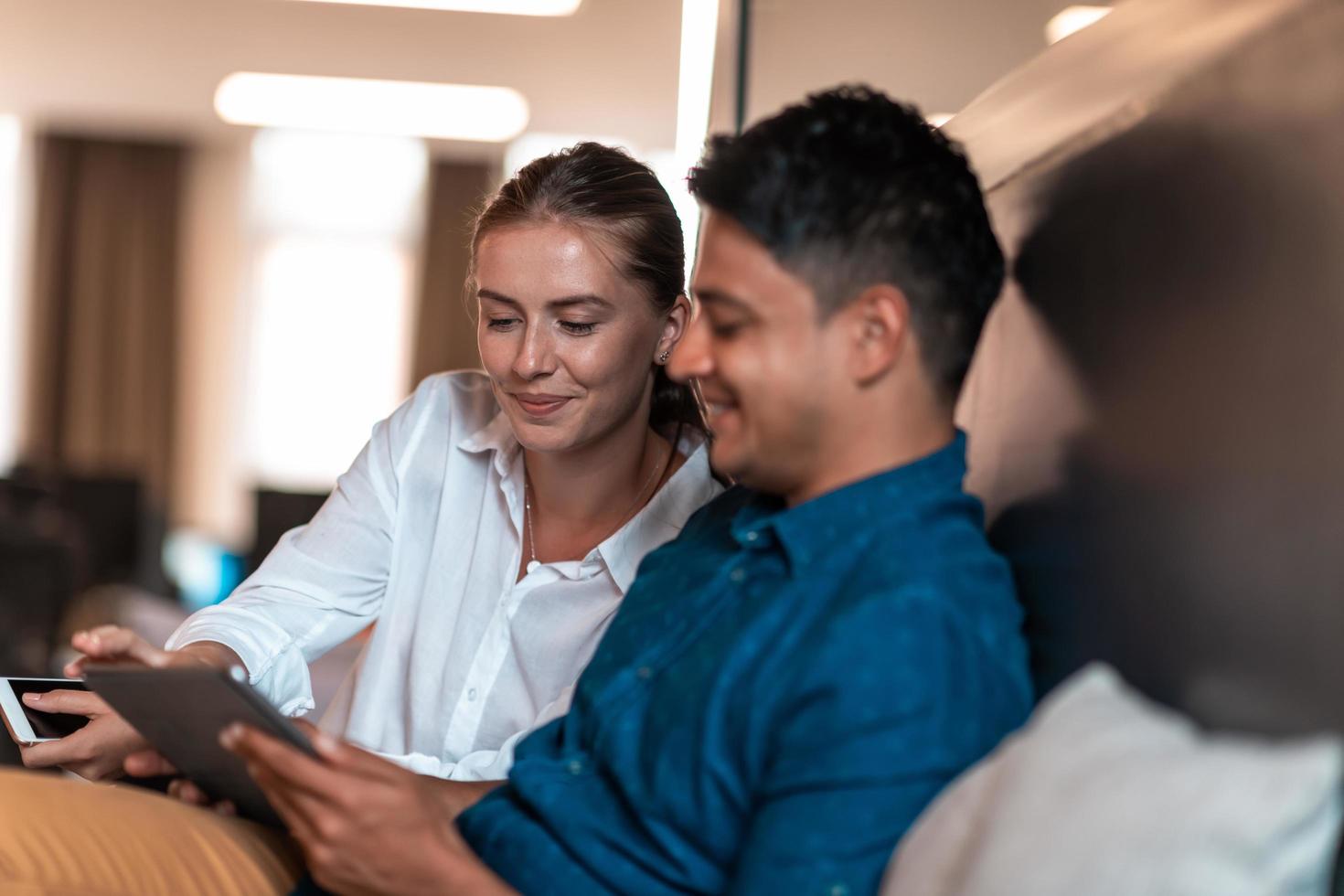 Multiethnic business people man with a female colleague working together on tablet computer in relaxation area of modern startup office photo