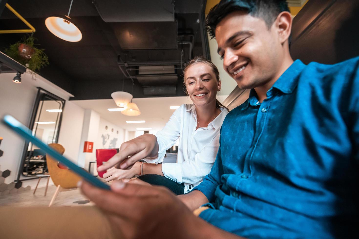 Multiethnic business people man with a female colleague working together on tablet computer in relaxation area of modern startup office photo