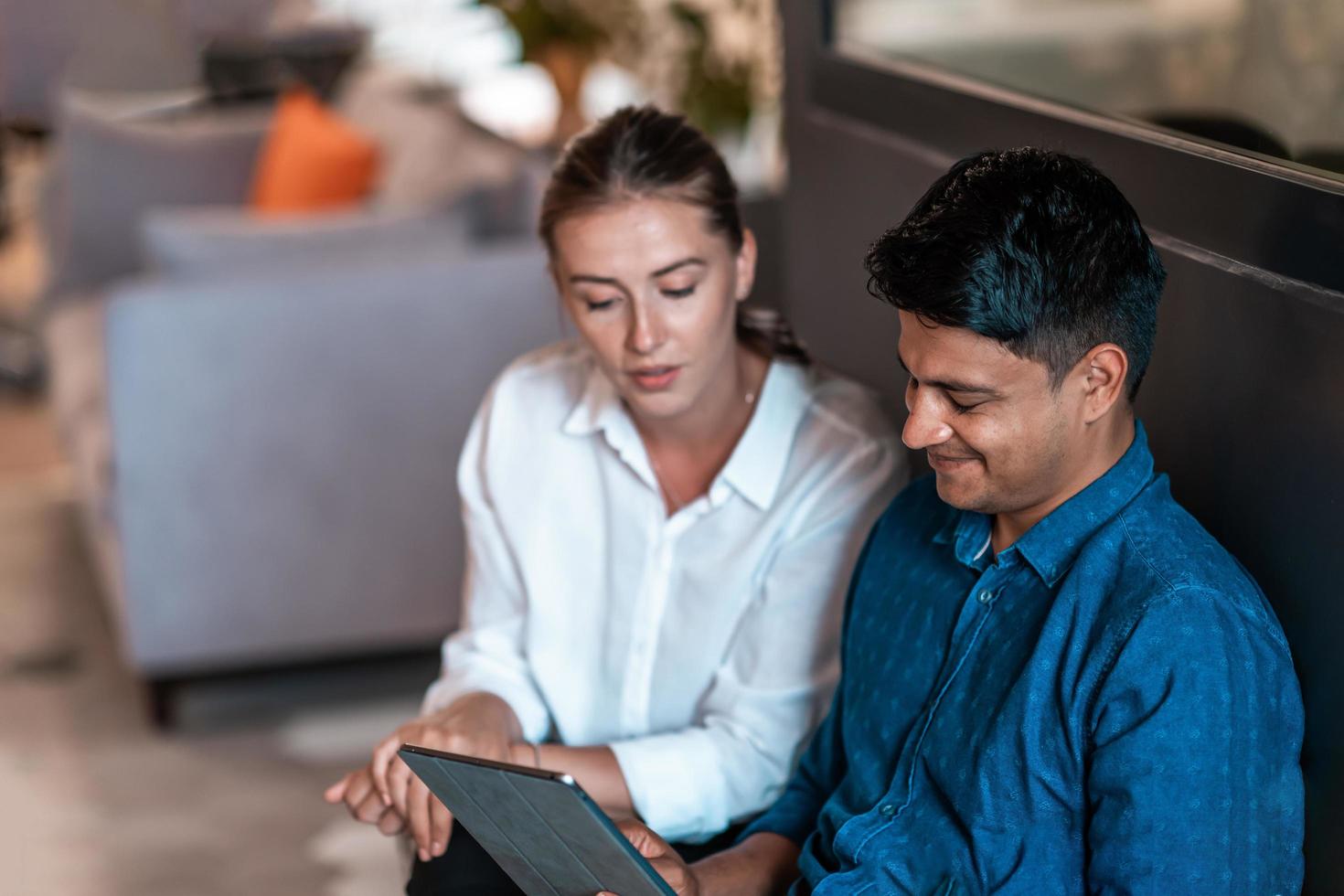 Multiethnic business people man with a female colleague working together on tablet computer in relaxation area of modern startup office photo