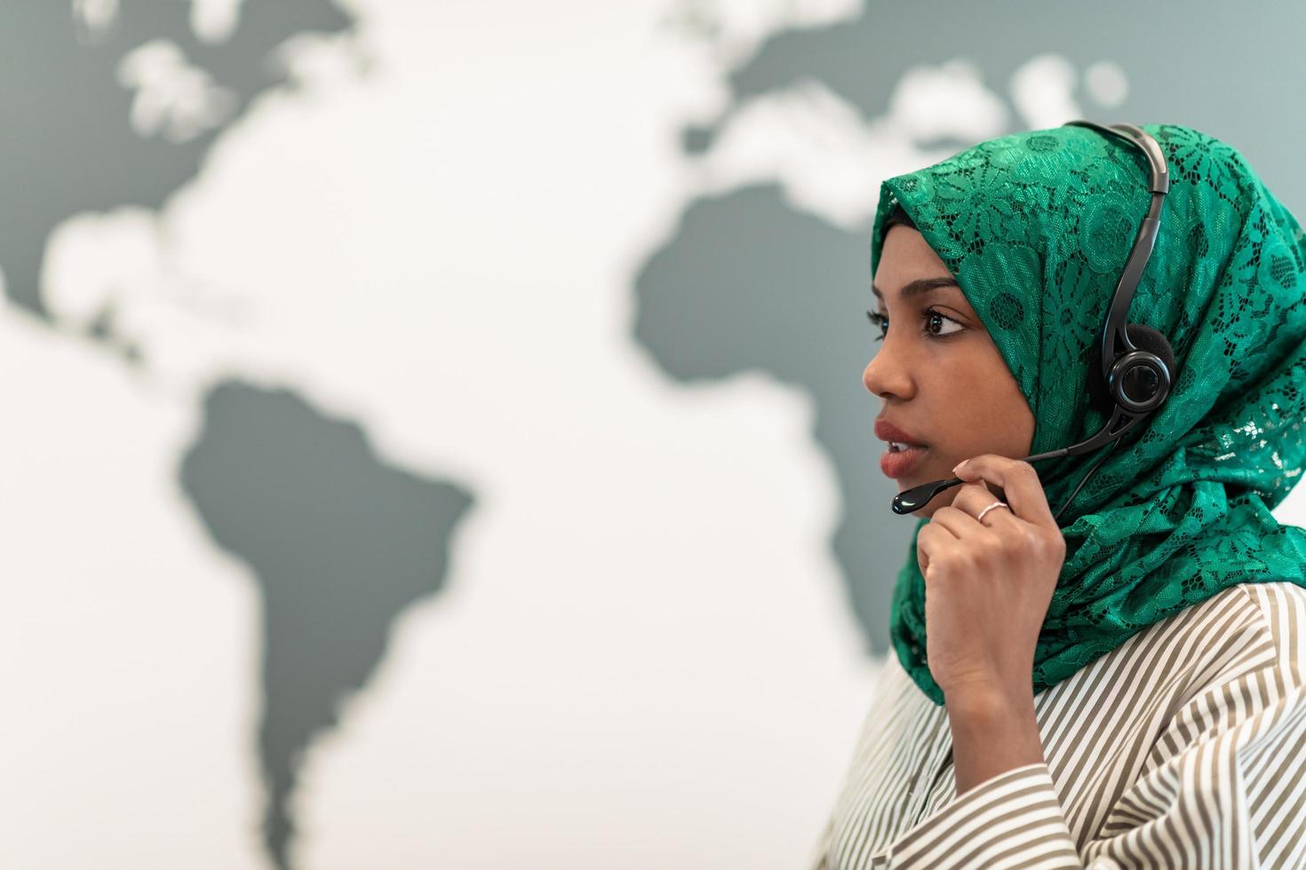 Afro Muslim female with green hijab scarf customer representative business woman with phone headset helping and supporting online with customer in modern call centre photo