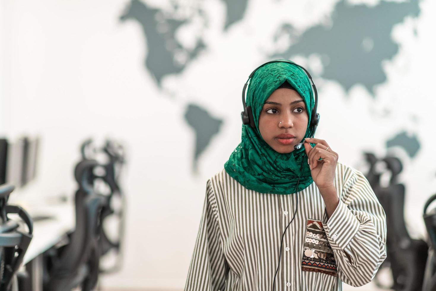 Afro Muslim female with green hijab scarf customer representative business woman with phone headset helping and supporting online with customer in modern call centre photo