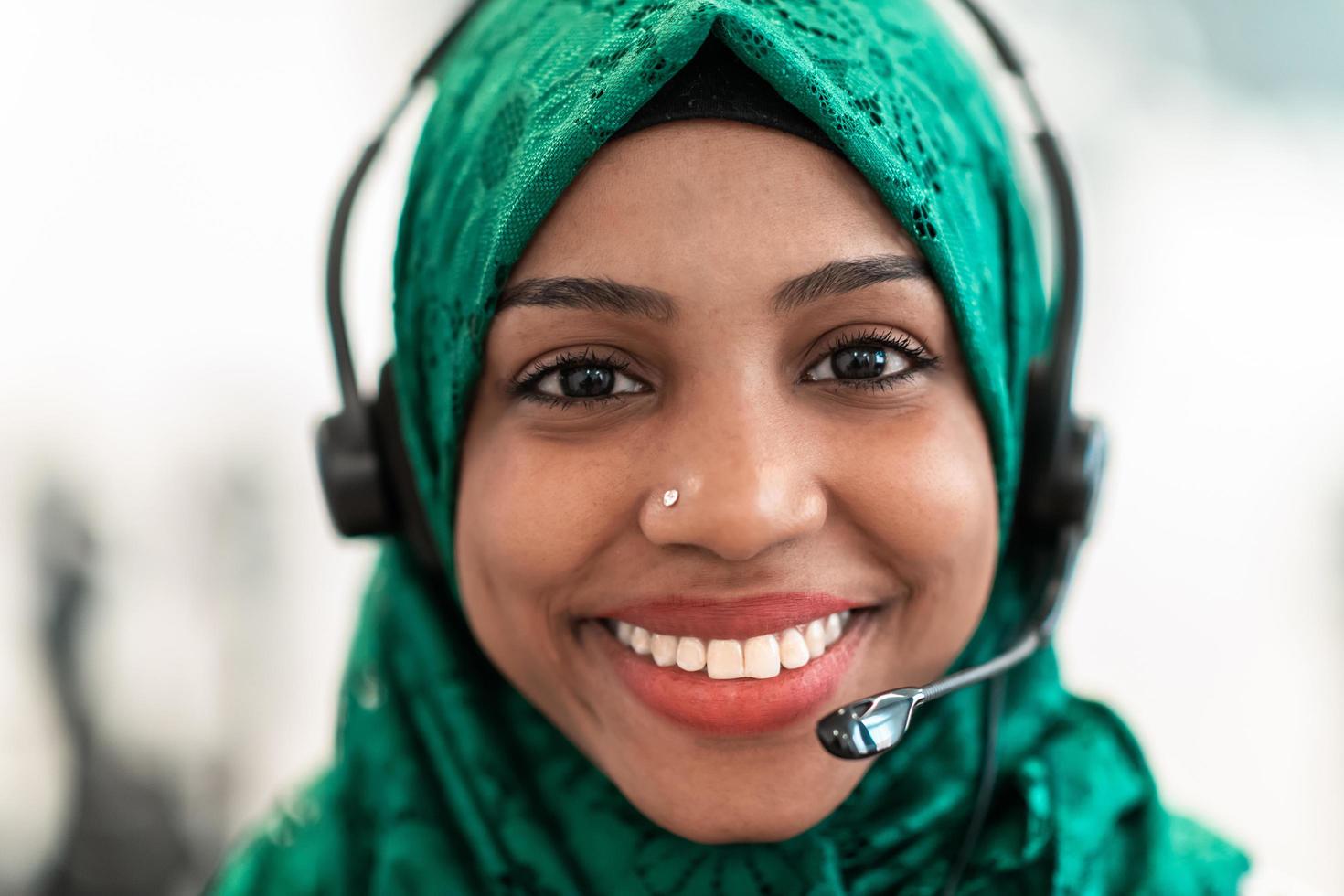 Afro Muslim female with green hijab scarf customer representative business woman with phone headset helping and supporting online with customer in modern call centre photo