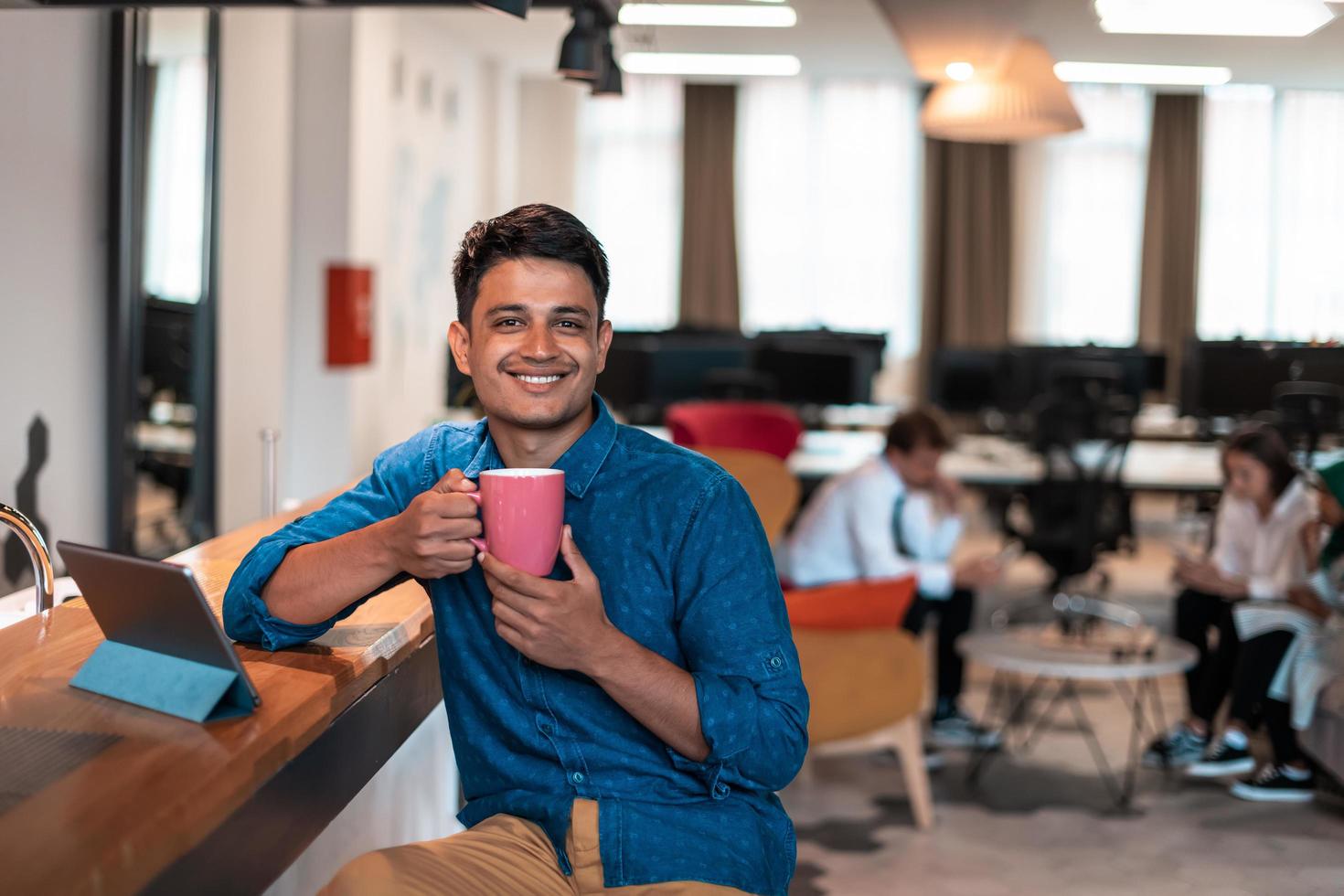 Casual business man taking break from the work using laptop while drinking tea in relaxation area of modern open plan startup office photo