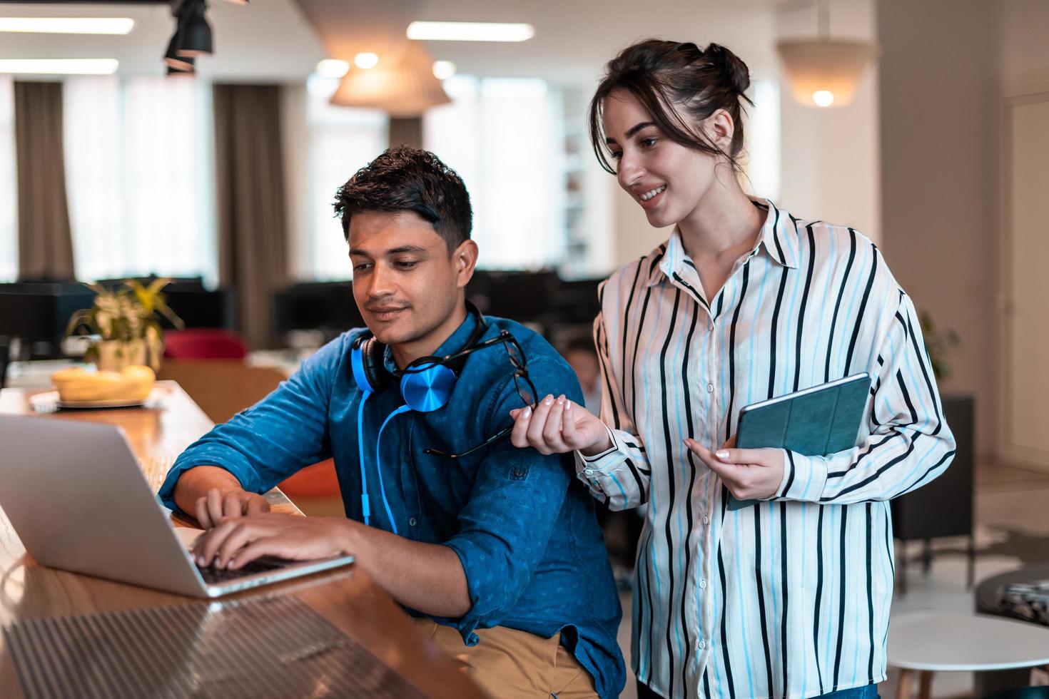 Multiethnic business people man with a female colleague working together on tablet and laptop computer in relaxation area of modern startup office photo