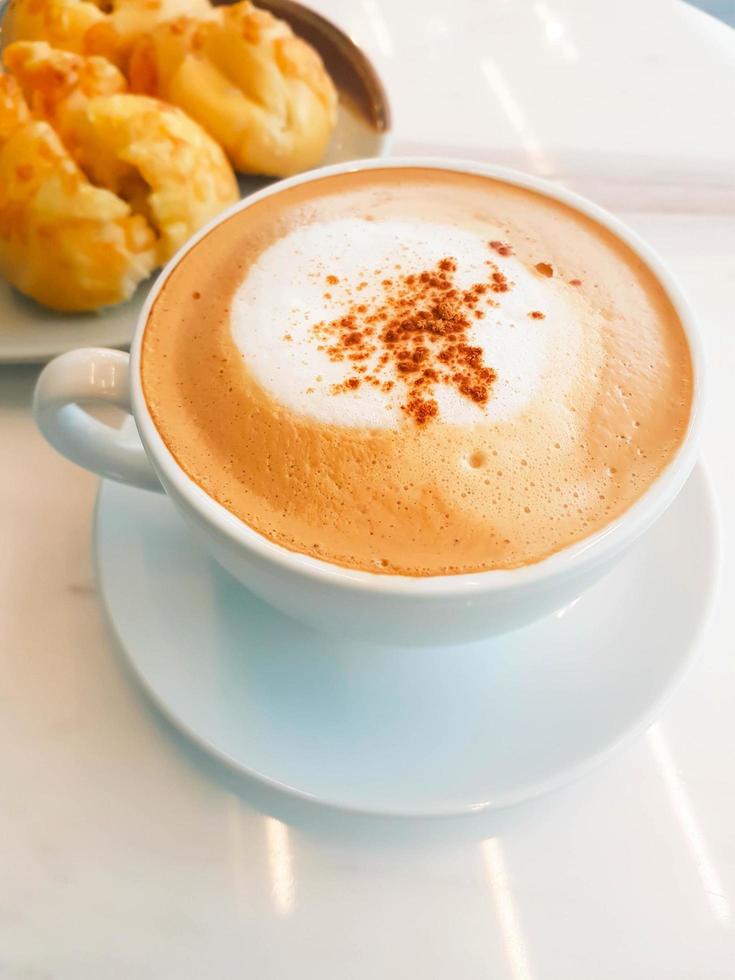 una taza de capuchino caliente y bollos de jamón y queso en un plato sobre una mesa blanca. foto