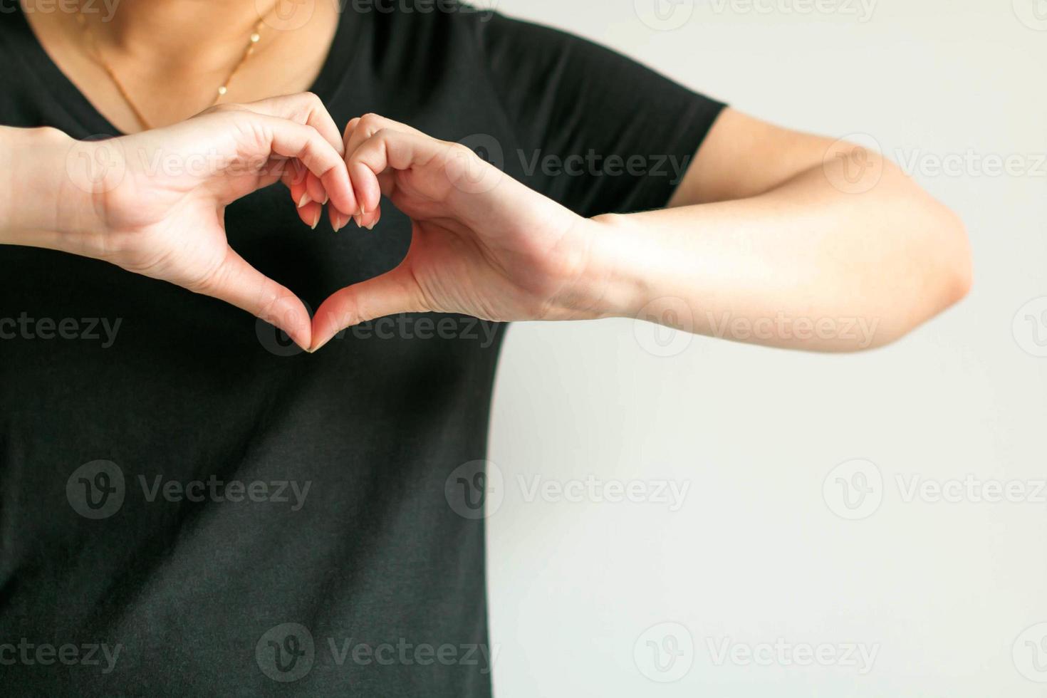 una mujer usa las manos para mostrar el símbolo del amor uniendo las yemas de los dedos para formar un lugar en forma de corazón en la parte delantera del pecho izquierdo. foto