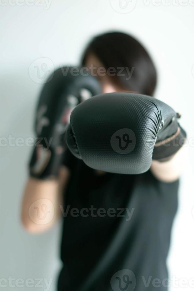 una mujer con guantes de boxeo negros estirando su puño izquierdo hacia el objetivo delantero. foto
