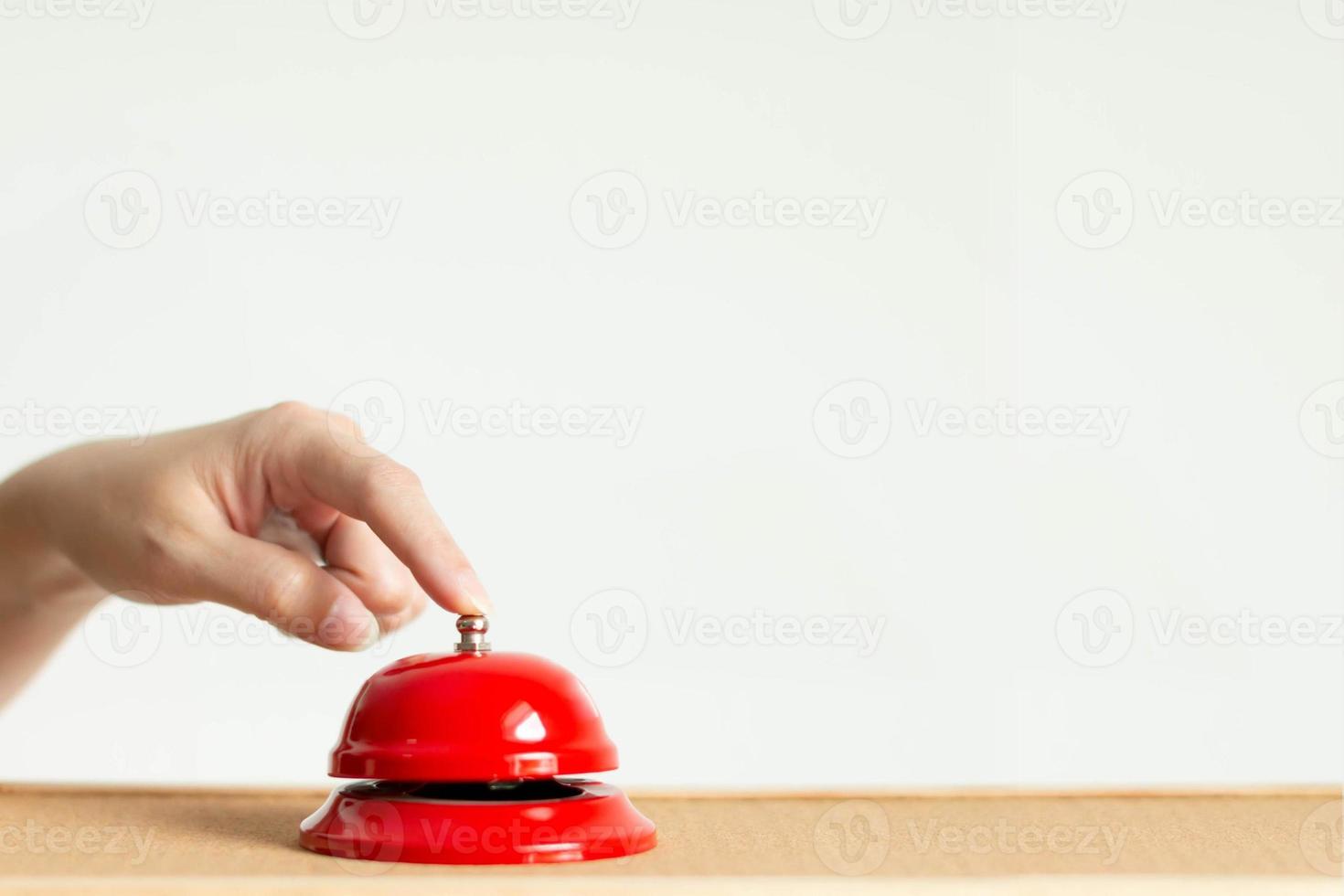 Close-up of index finger pressing the bell button of red vintage style handbell on wooden table. photo