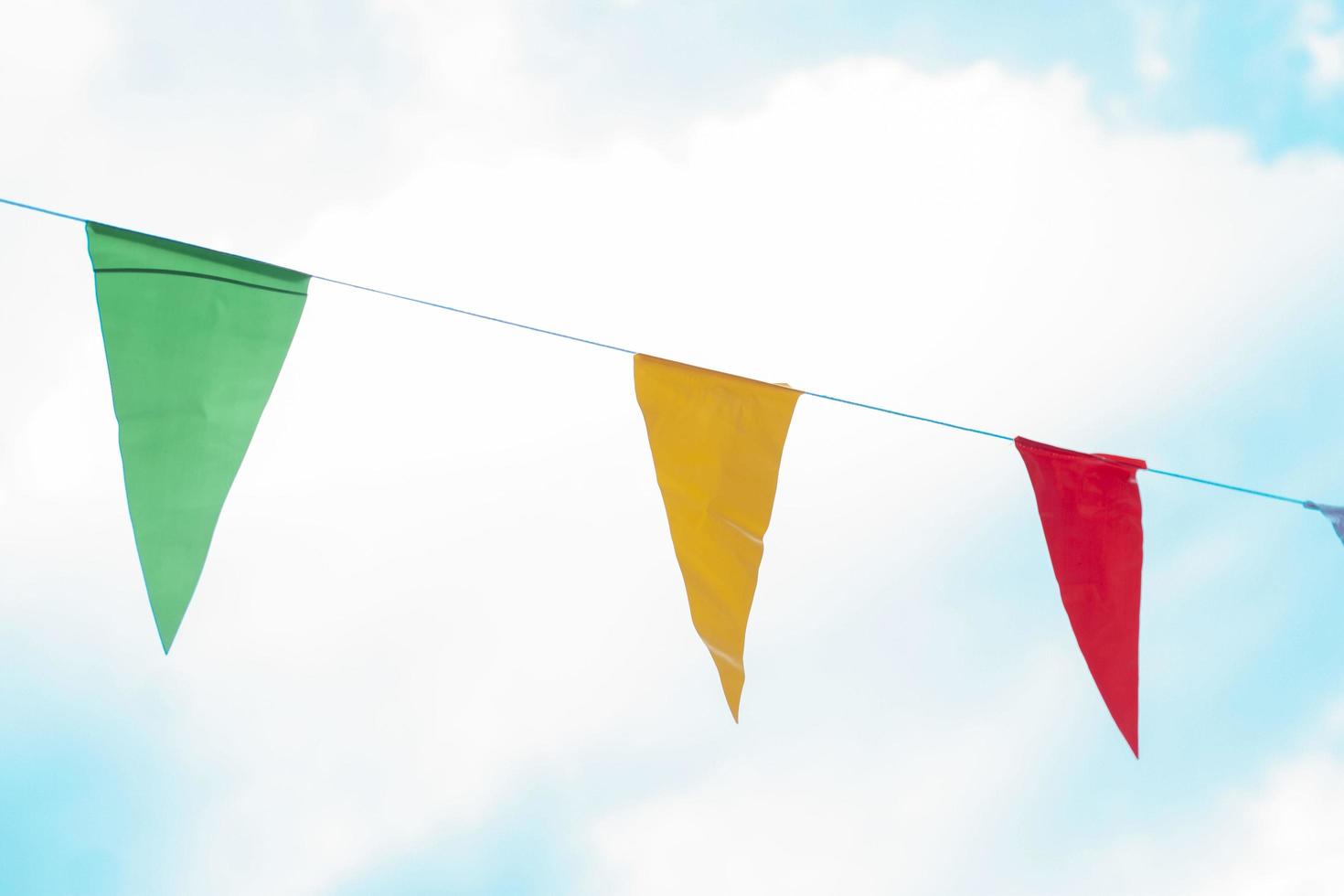 Various colors flags hanging on a rope on white clouds and blue sky background. photo