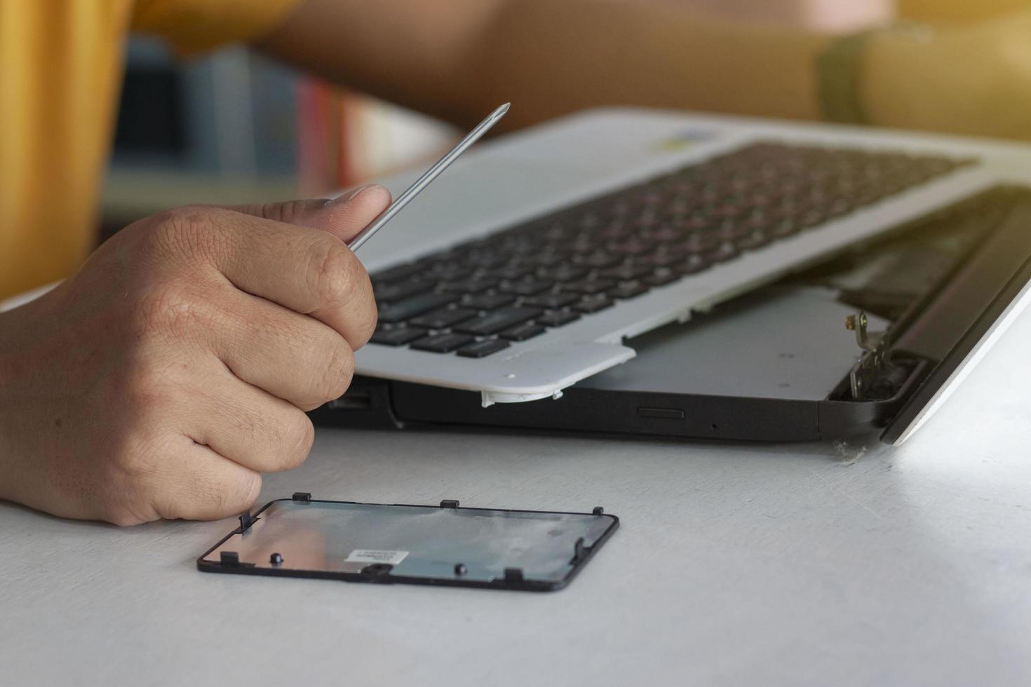 The hand of the mechanic is holding a screwdriver to fix the laptop computer. photo