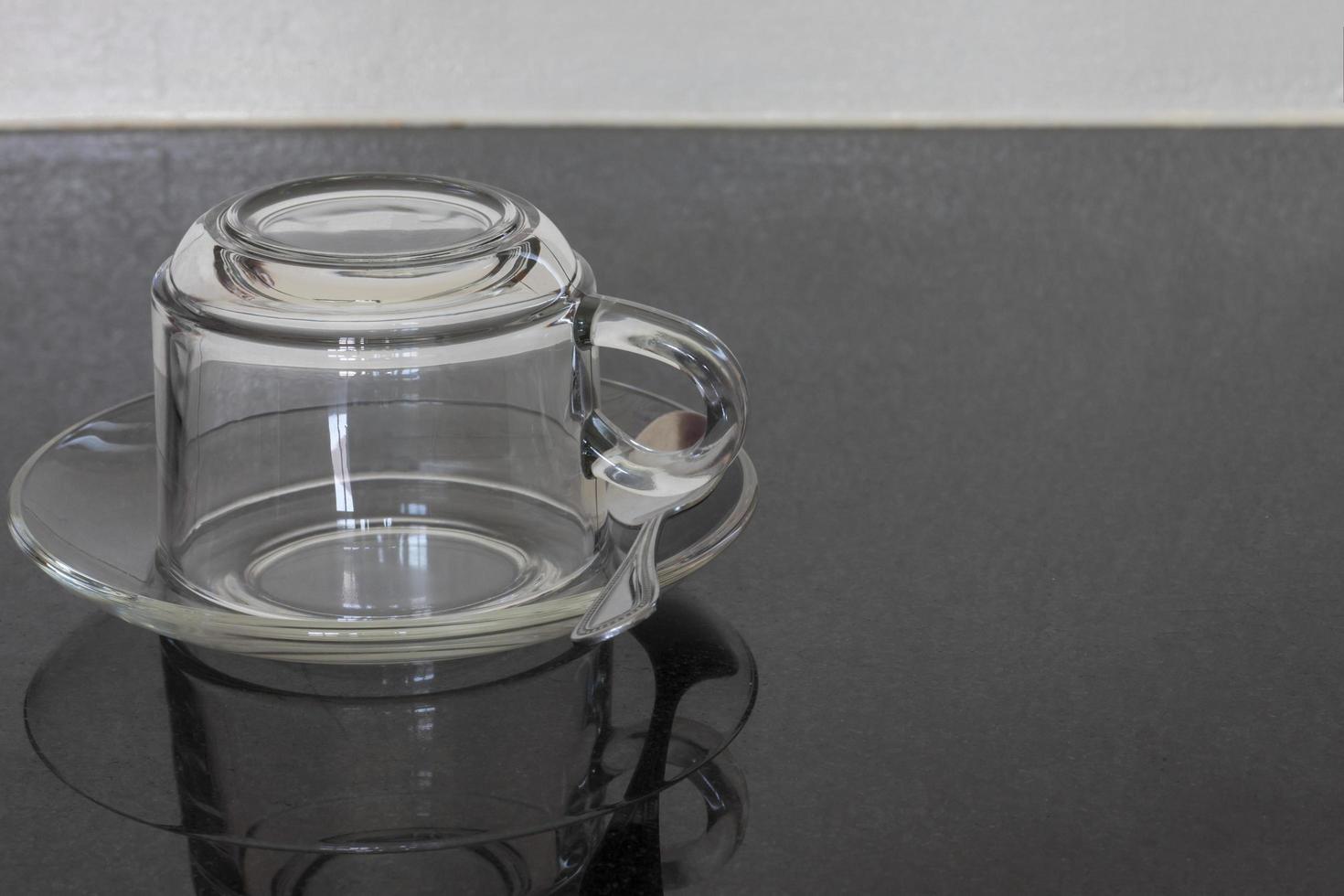 Empty upside down transparent coffee cup on a clear plate with a spoon on the table. photo