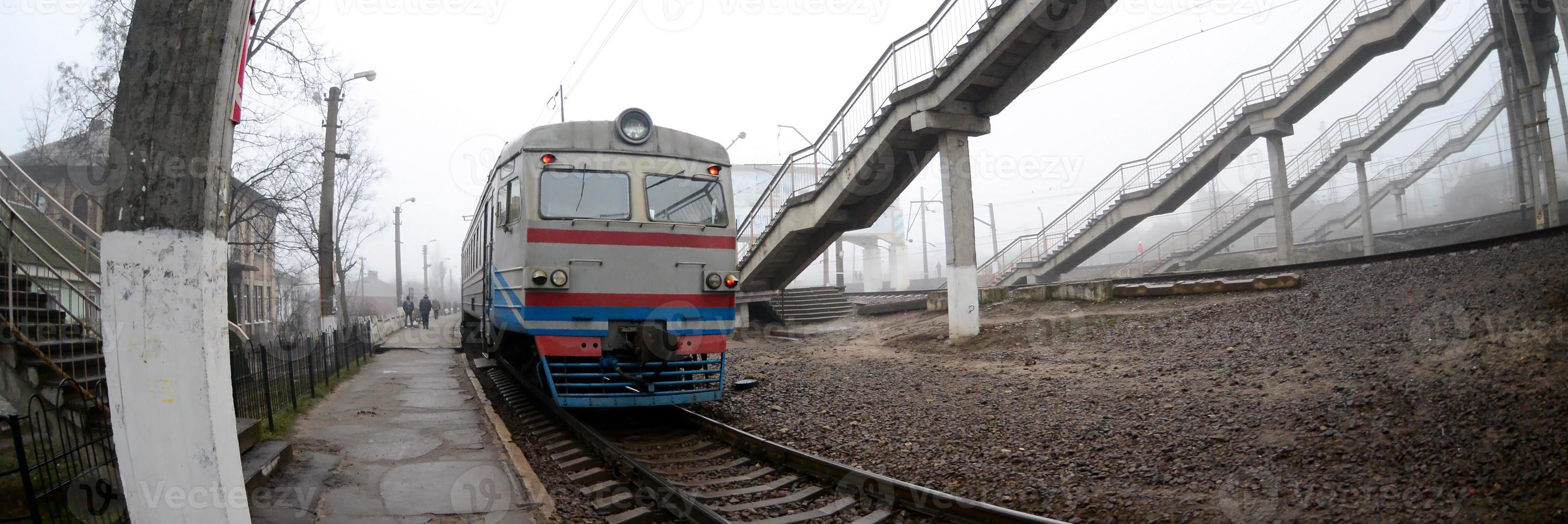 The railway track in a misty morning. The Ukrainian suburban train is at the passenger station. Fisheye photo with increased distortion