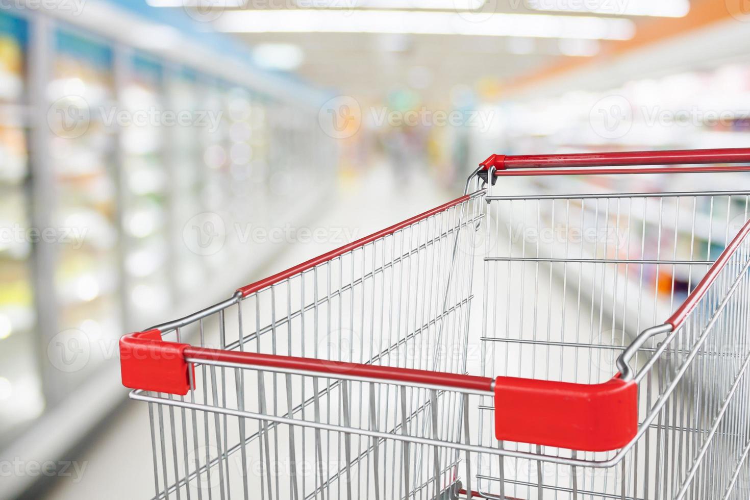 Supermarket aisle blur defocused background with empty red shopping cart photo