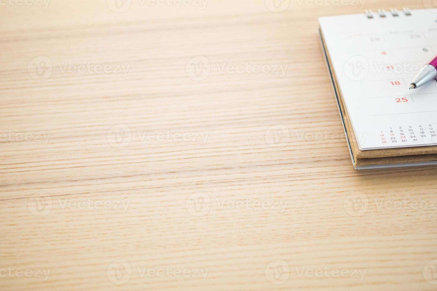 calendar page with pen point at 25th date on wood table background photo