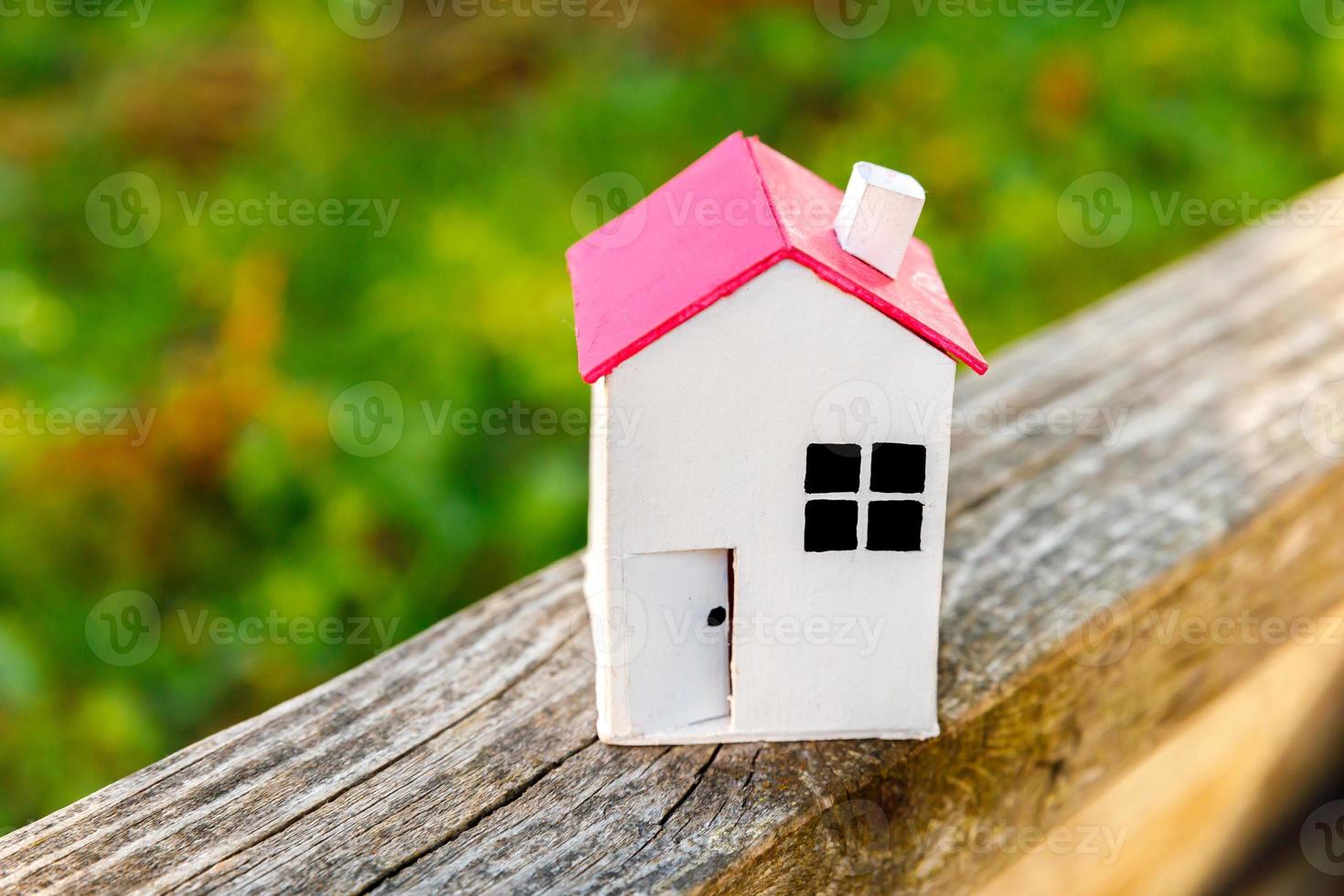 Miniature white toy model house in wooden background near green backdrop. Eco Village, abstract environmental background. Real estate mortgage property insurance dream home ecology concept. photo