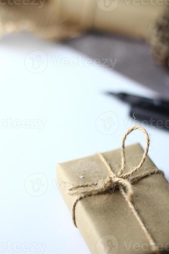 regalos de vacaciones caja de regalo de navidad y año nuevo envuelto en papel marrón, piñas y papel blanco y bolígrafos colocados en el espacio de copia de la mesa. foto