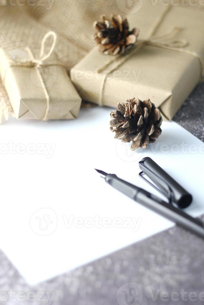 regalos de vacaciones caja de regalo de navidad y año nuevo envuelto en papel marrón, piñas y papel blanco y bolígrafos colocados en el espacio de copia de la mesa. foto