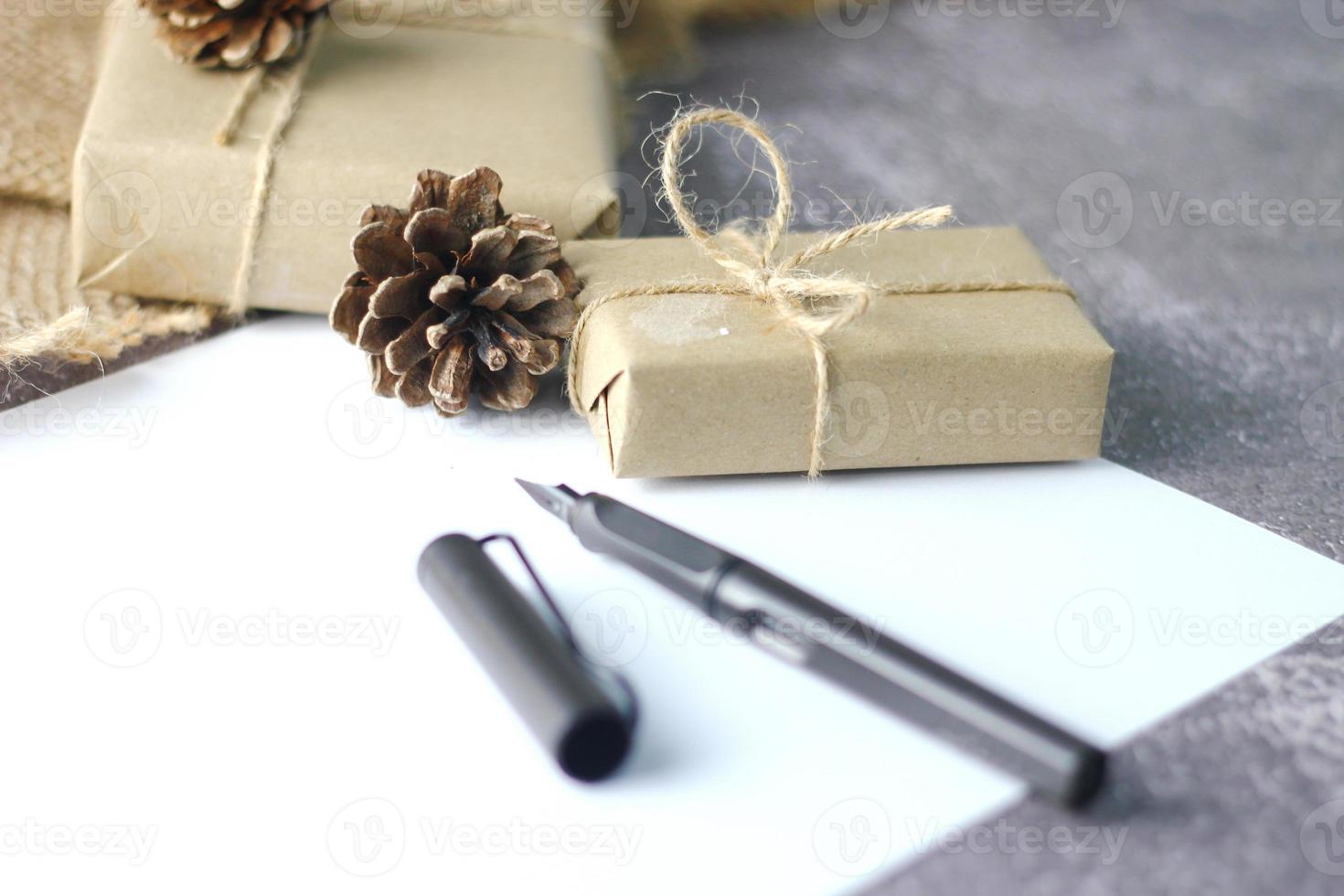 Holidays Gifts Christmas and New Year Gift box wrapped in brown paper, pine cones and white paper and pens placed on the table copy space. photo