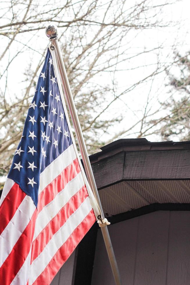 The American flag in front of the house against the backdrop of a leafless tree in winter. photo