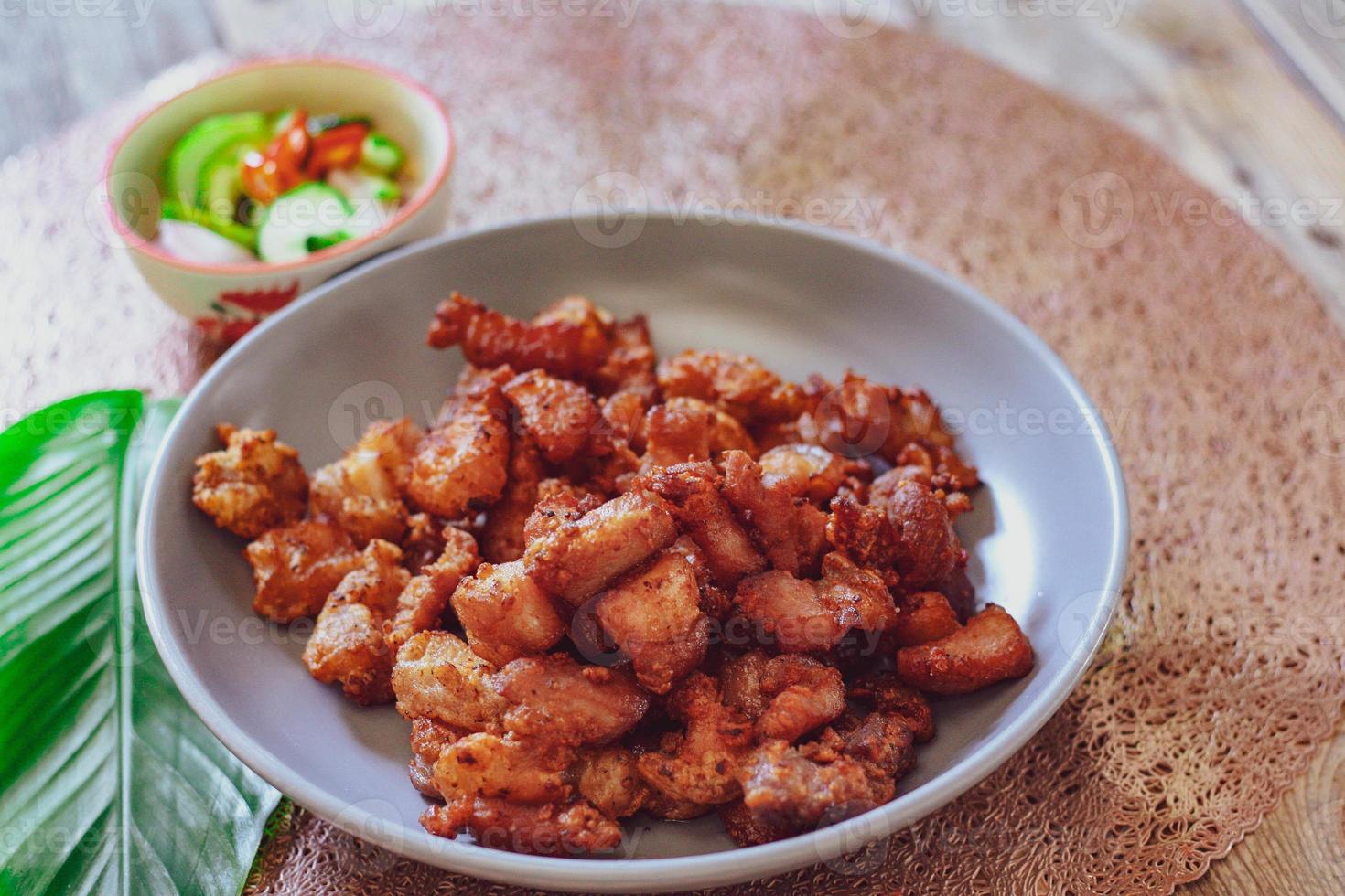Fried Pork Belly with Fish Sauce and Sticky Rice Served on a white plate on a black wooden floor. photo