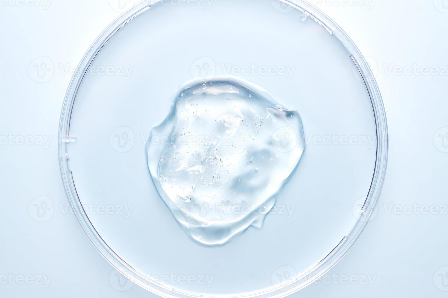 Petri dish with gel or cosmetic liquid on blue background closeup. Transparent container with gel with bubbles. Texture of the gel. Medicine and beauty concept. Medical glassware for laboratories photo