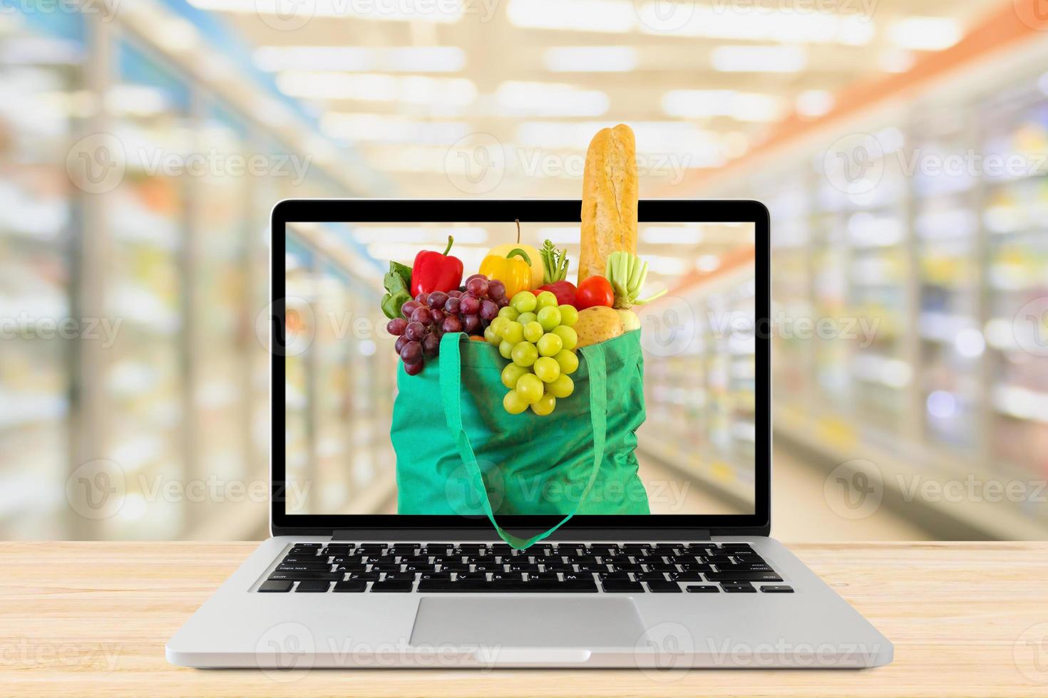 supermarket aisle blurred background with laptop computer and green shopping bag on wood table grocery online concept photo