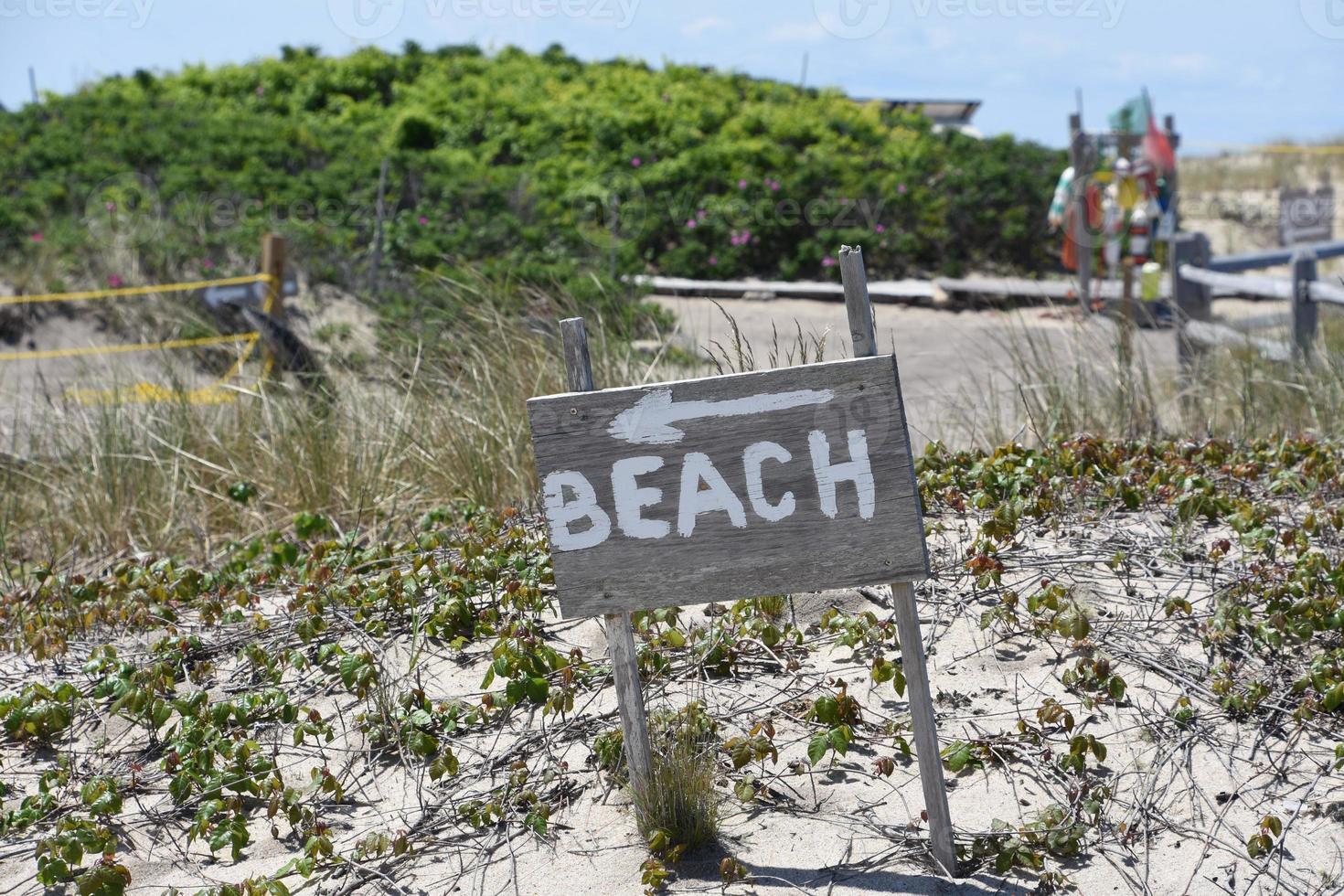 cartel de playa de madera con una flecha en la arena foto