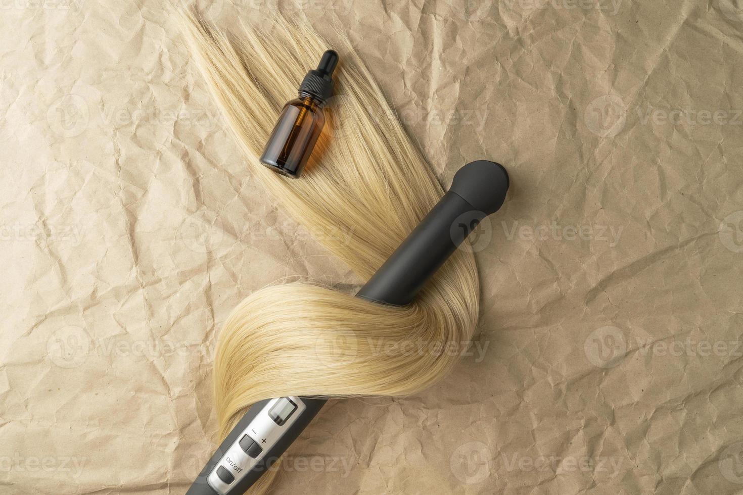 A hair treatment essential oil for smoothing hair and a hair curling styler lying on a brown craft paper background photo