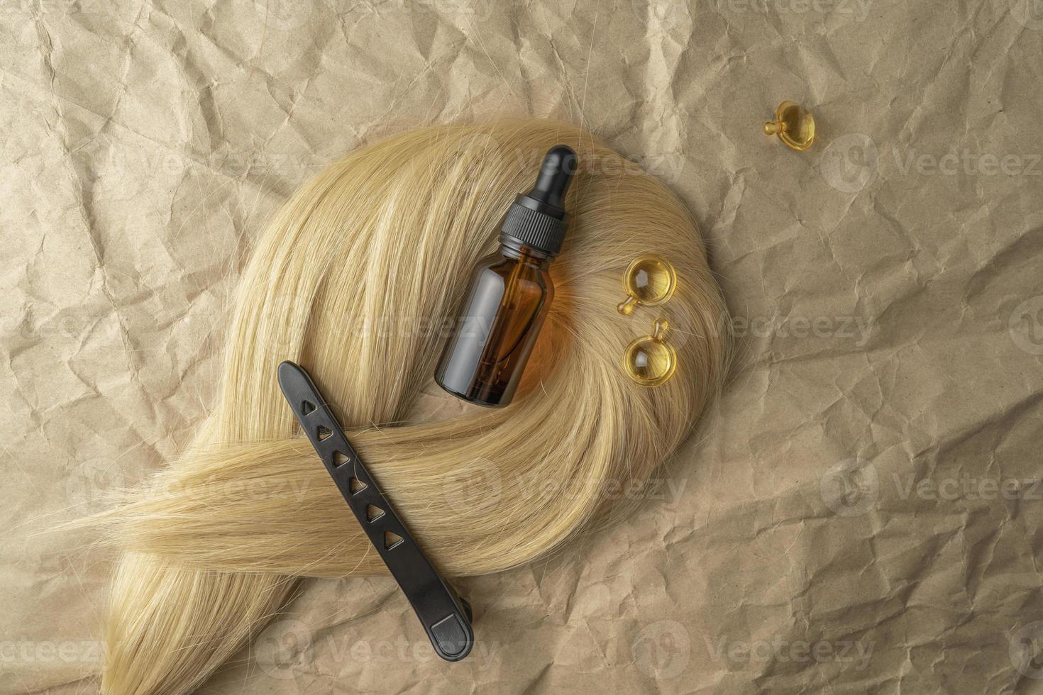 A hair treatment essential oil for smoothing hair and a hair curling styler lying on a brown craft paper background photo